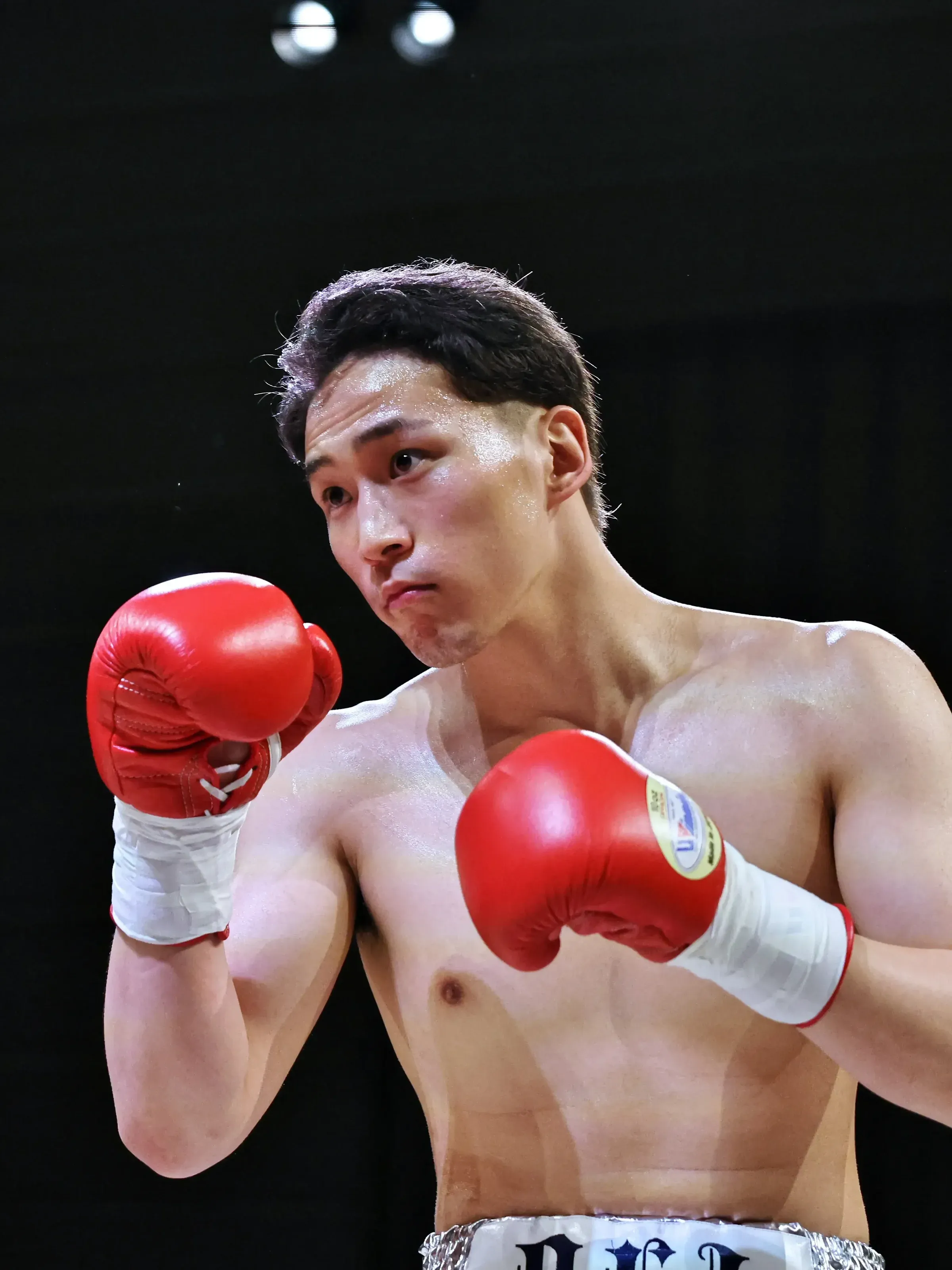 赤いグローブを構えるフュチュールボクシングジムの選手。左手前に相手の青いグローブ